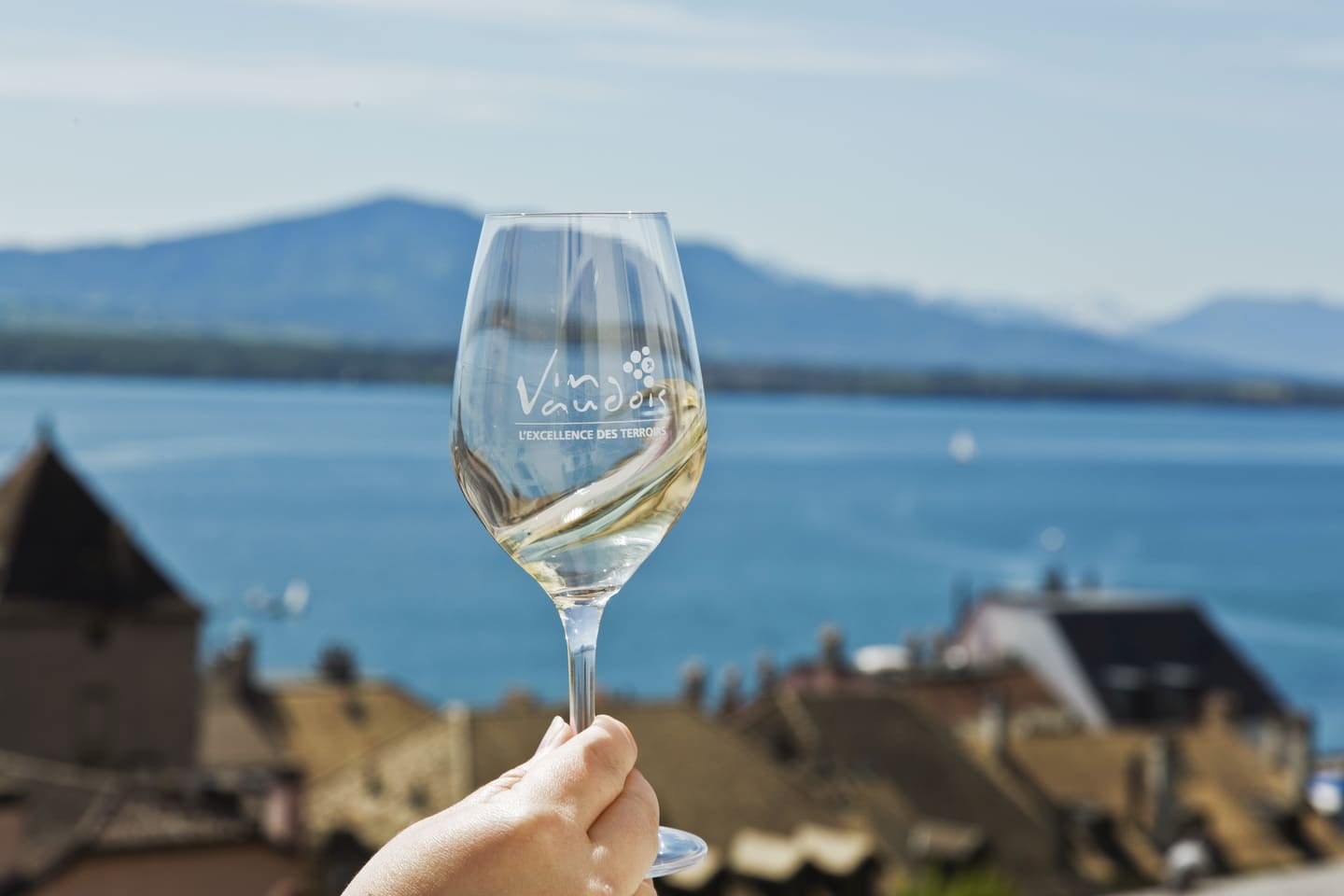 Main qui tien un verre de Chasselas avec le lac Léman en arrière plan